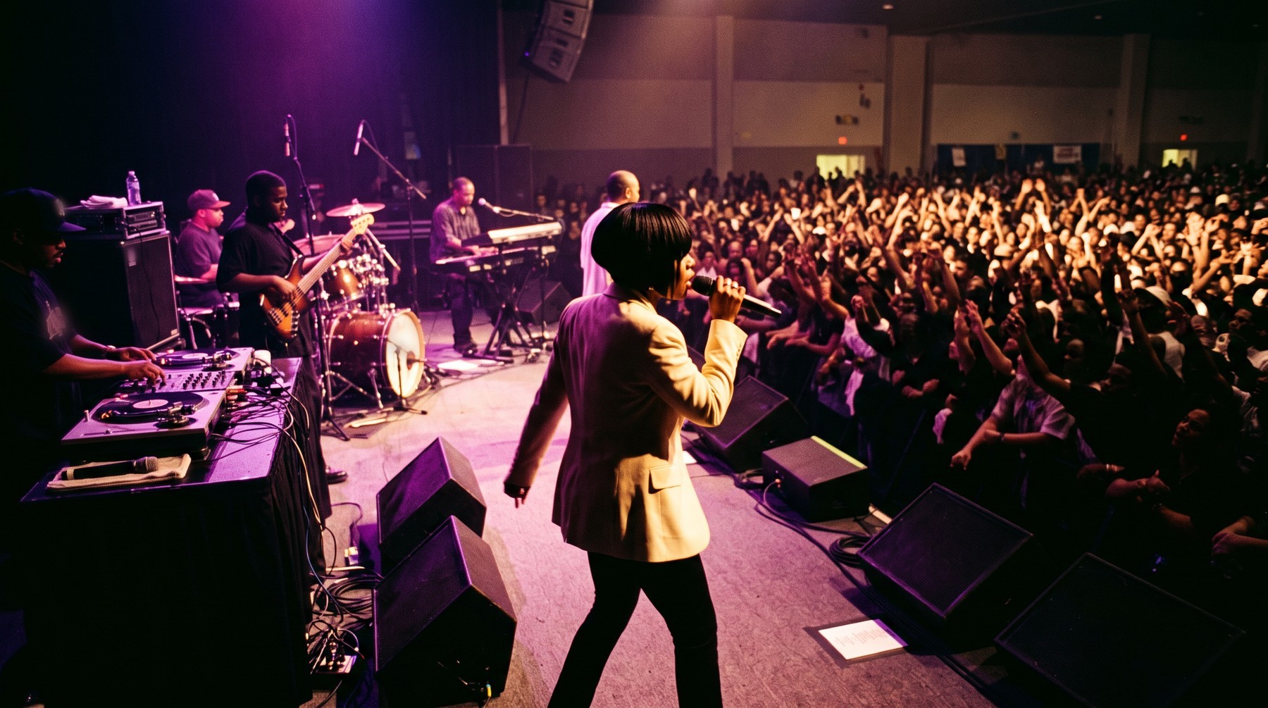 The singer in a cream blazer, seen from behind on stage, faces a large crowd with raised hands